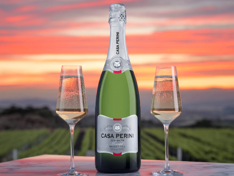 Garrafa de Casa Perini Moscatel, 5º melhor vinho do mundo, com taça de espumante borbulhante ao lado em cenário de vinhedos.
