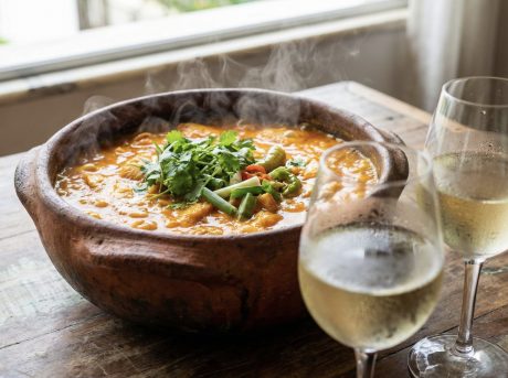 Panela de barro com moqueca brasileira fumegante ao lado de taças de vinho branco gelado, ilustrando que vinho combina com moqueca.