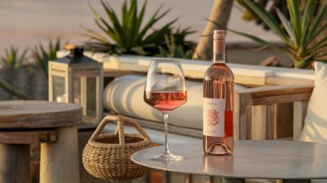 Taça de vinho rosé bom e barato sendo servida ao pôr do sol com garrafa ao lado